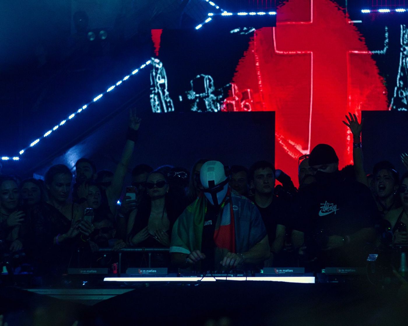 DJ booth under a glowing red neon cross and blue lasers