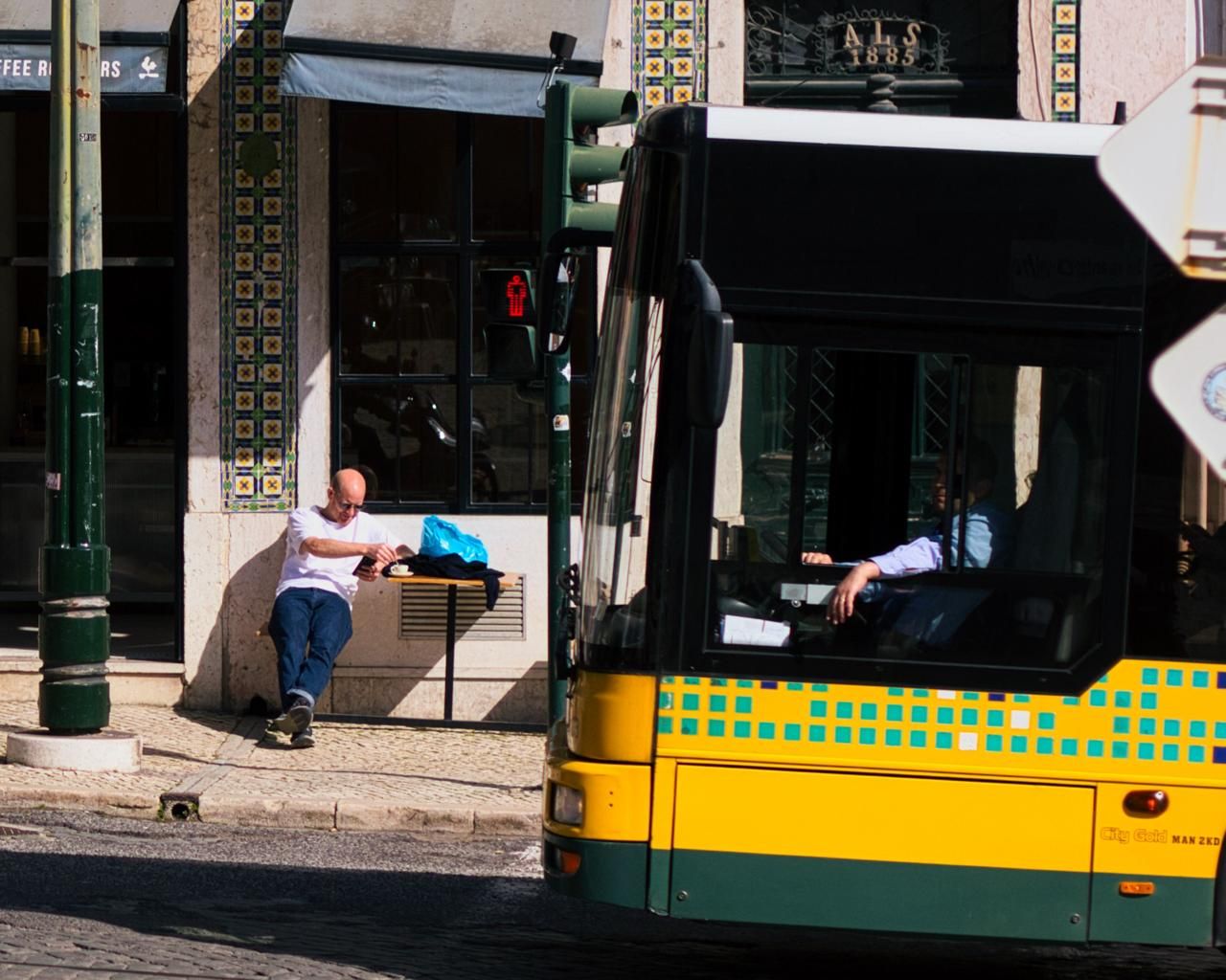Yellow bus beside a man resting on a bench