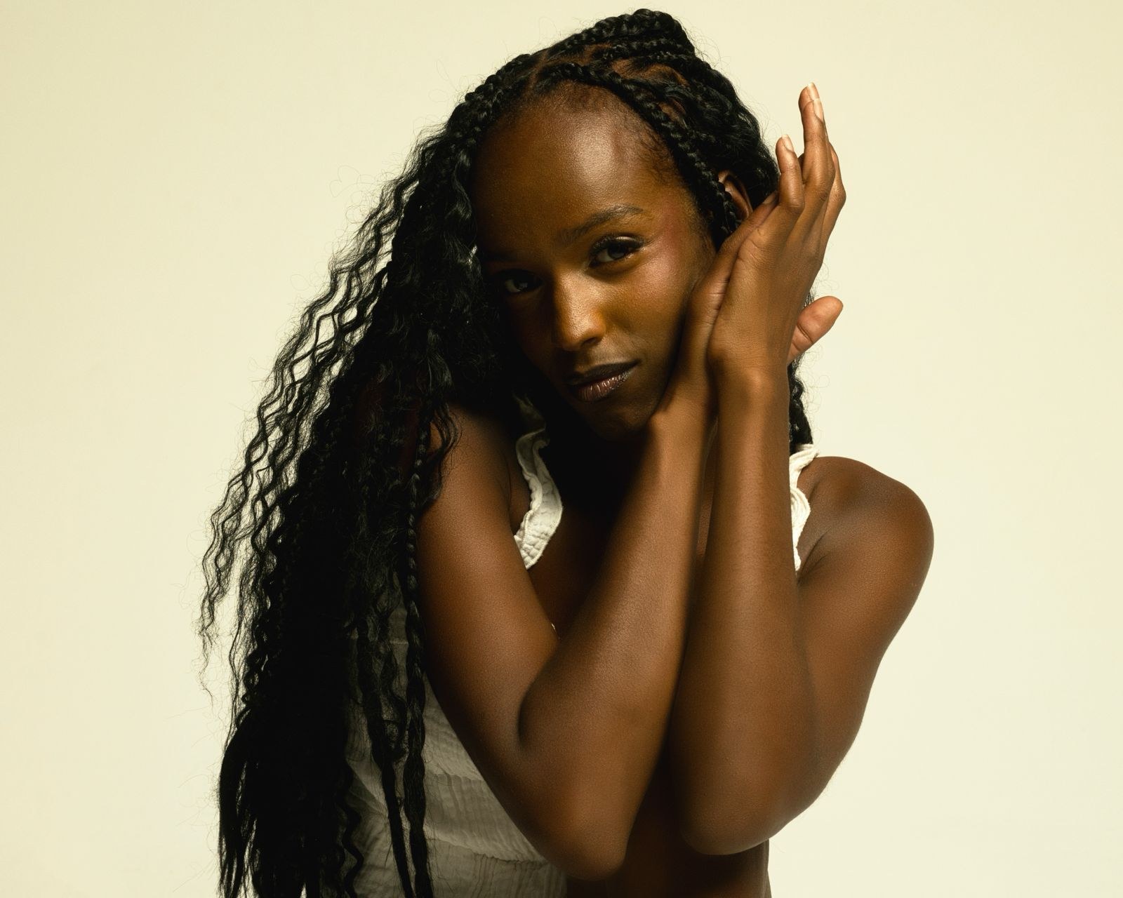 Woman with long braids and hands framing her face against a cream backdrop