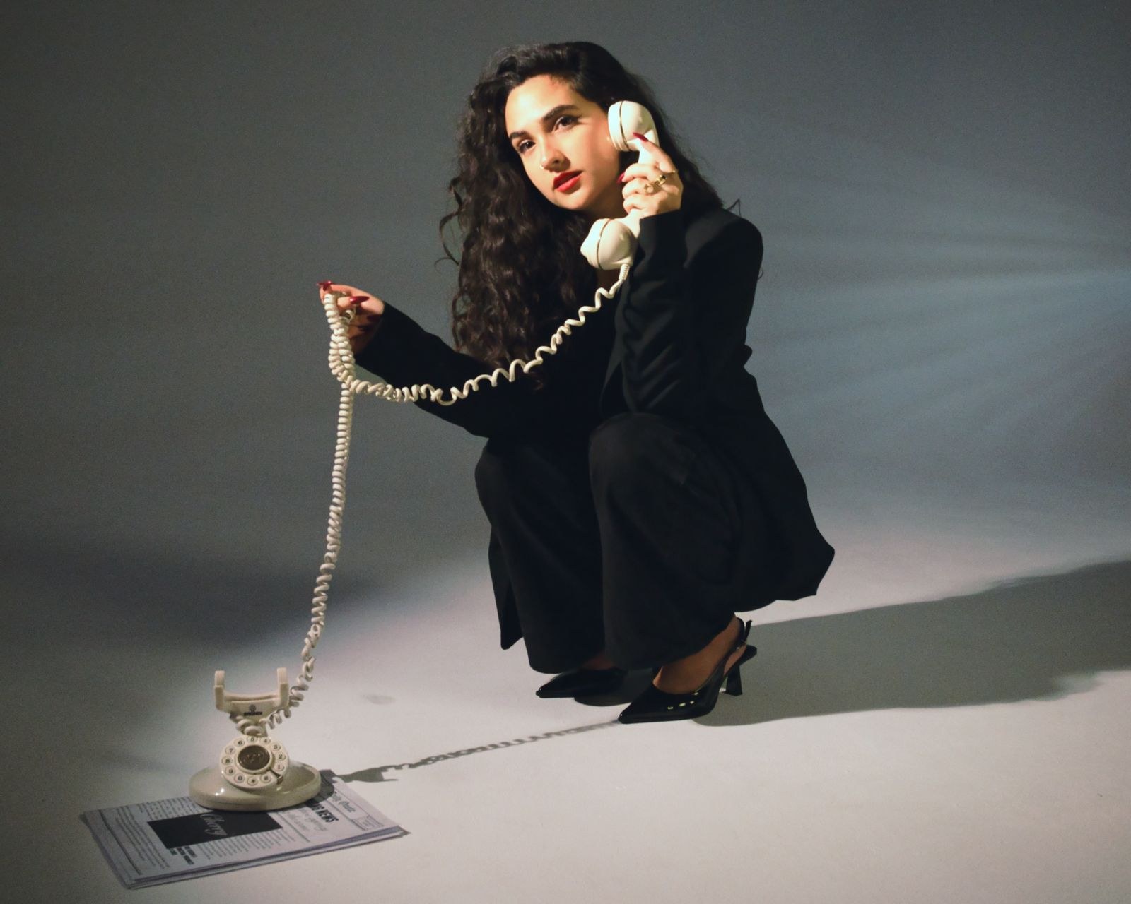 Woman crouching in a black suit with a vintage phone on a long cord