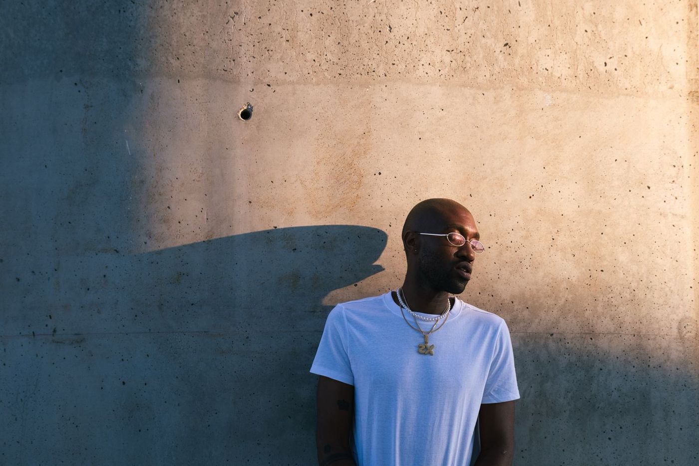 Man in a white t-shirt against a sunlit concrete wall