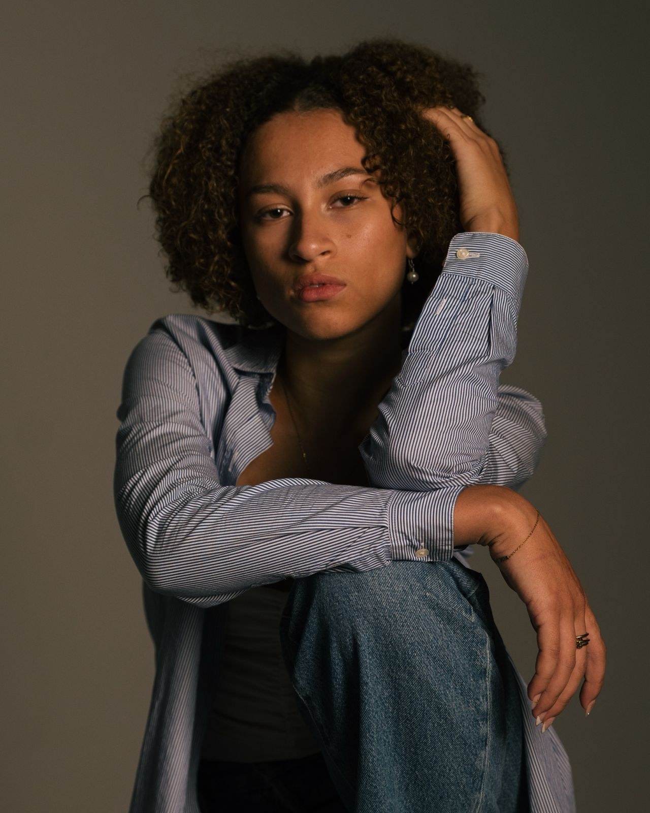 Woman in a blue shirt and jeans with a hand in her hair