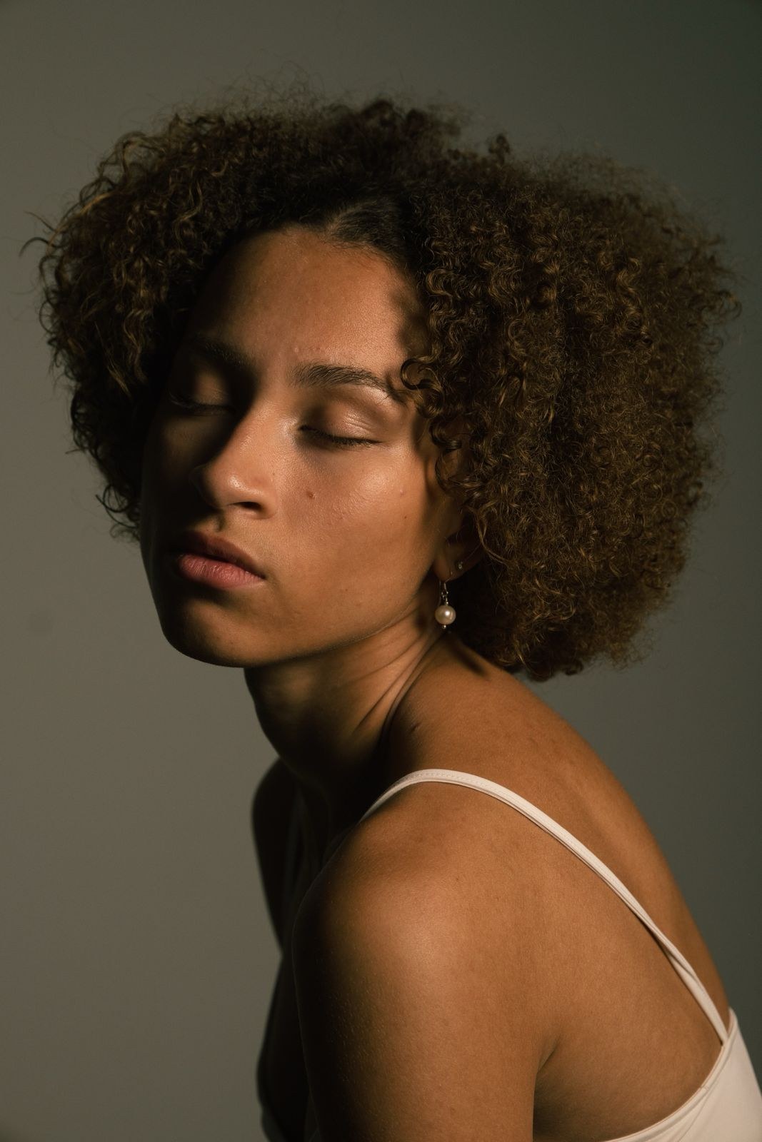 Woman with closed eyes and curly hair looking over her shoulder