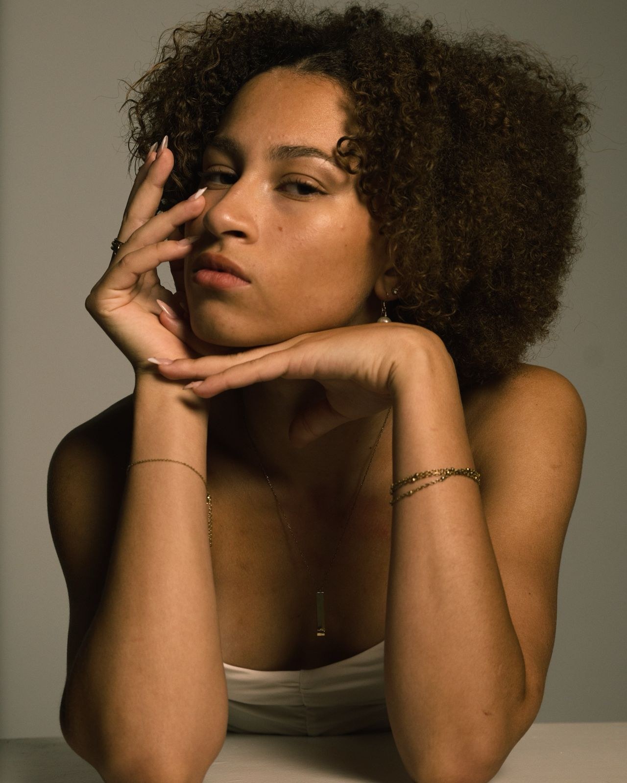 Woman with her chin on folded hands, curls lit from the side