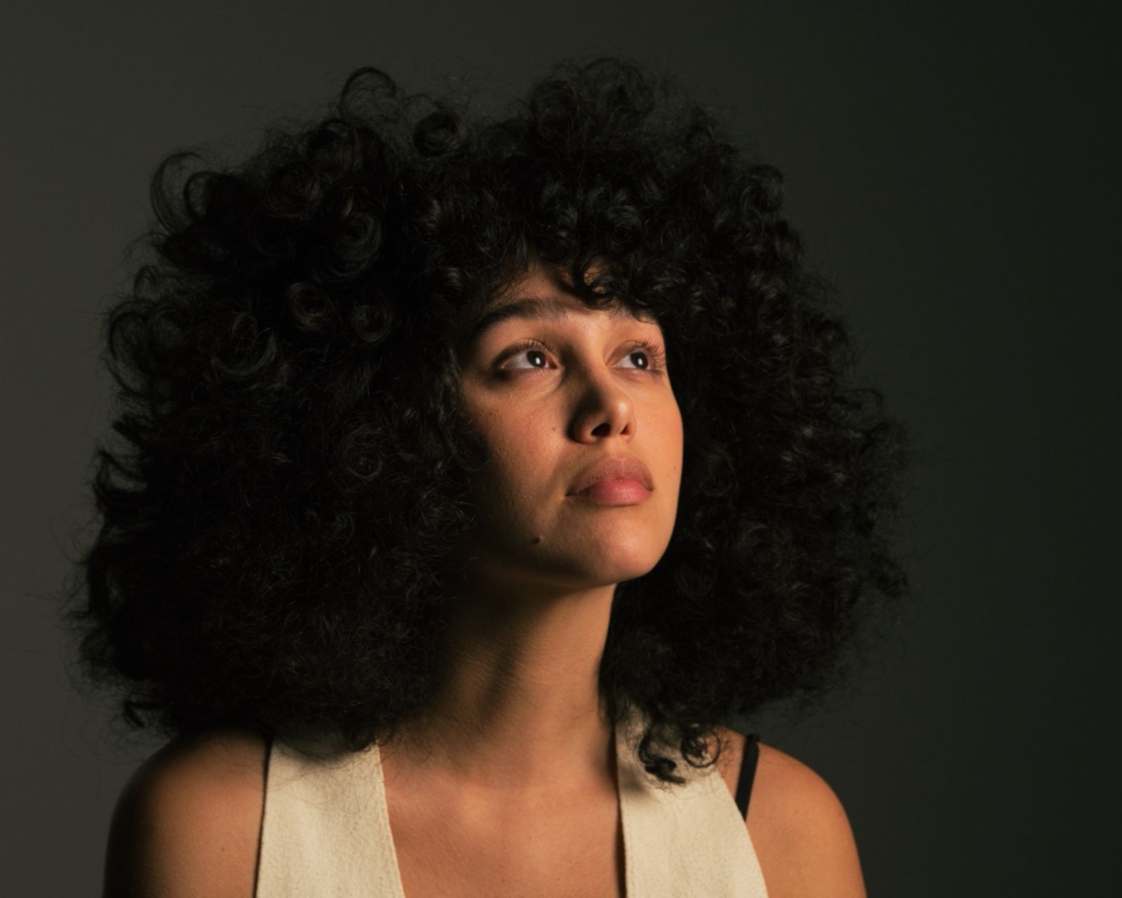 Portrait of a woman with voluminous curls looking up, in soft low light