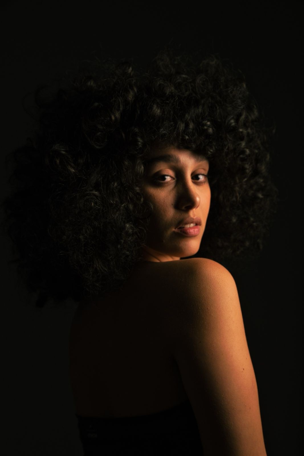 Woman with curls glancing over her shoulder in deep shadow