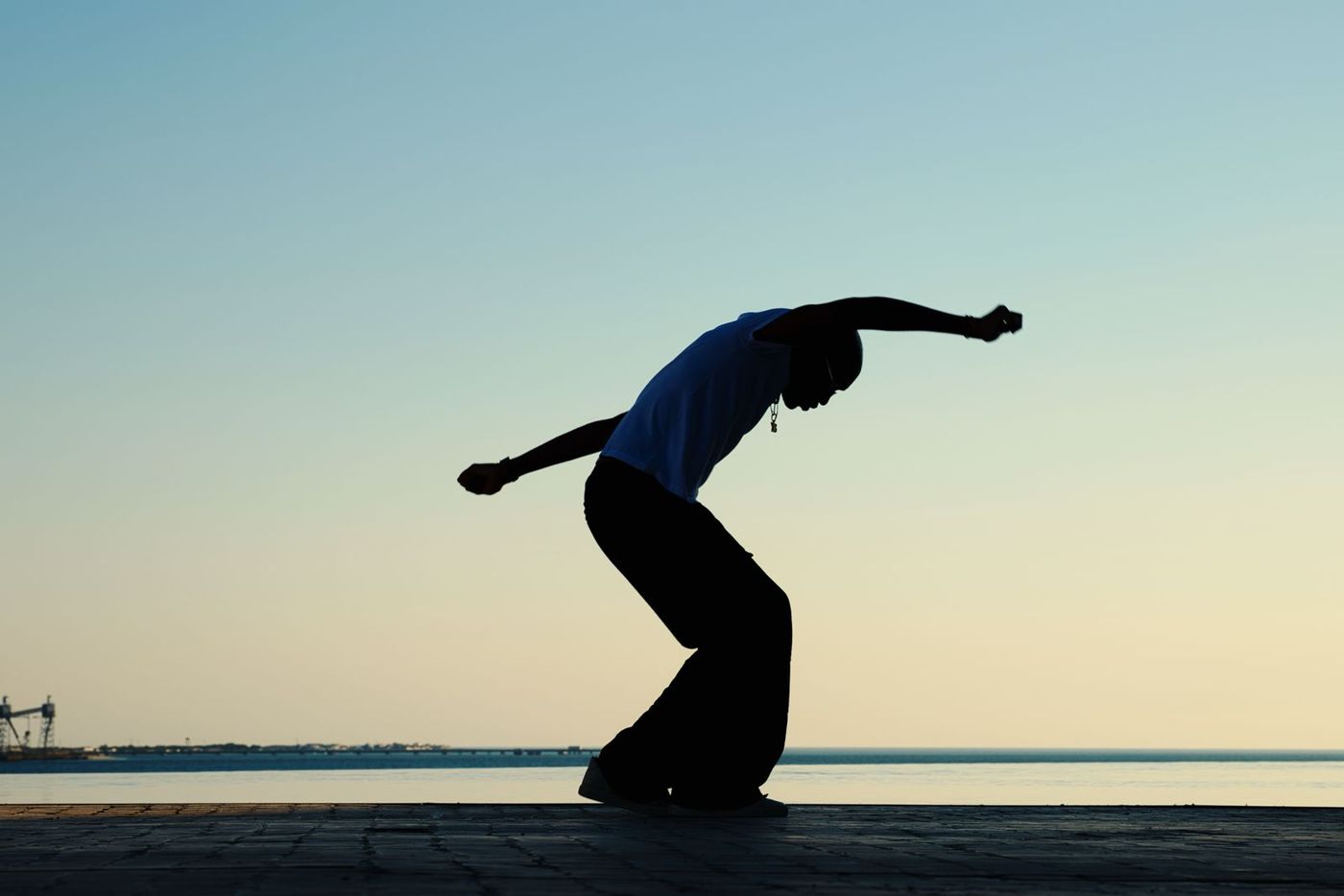 Silhouette of a dancer bending against a pale sunset sky